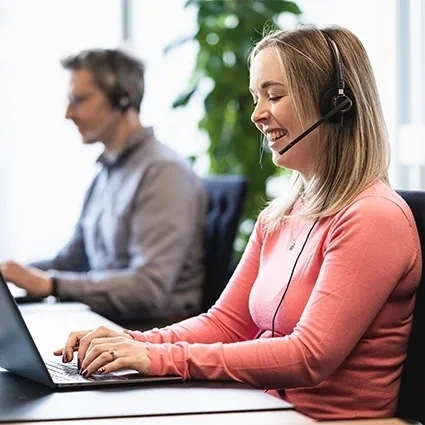 Zwei personen arbeiten an schreibtischen eine nutzt einen laptop mit headset und die andere im hintergrund trägt ebenfalls ein headset