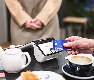 Person haelt visa karte nahe zahlungsterminal auf tisch mit kaffee teekanne und essen im cafe