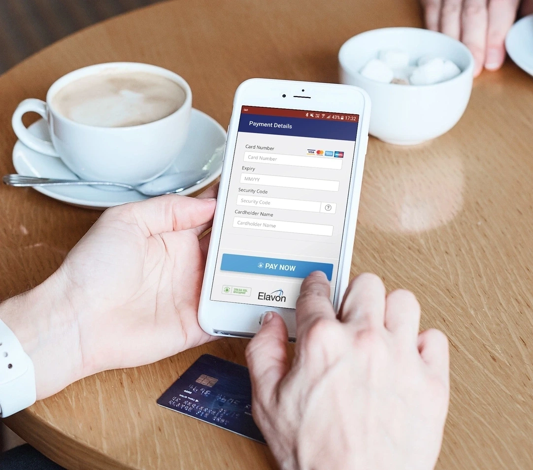 Person hält ein smartphone mit einem online zahlungsformular und einer kreditkarte auf einem tisch neben einer tasse kaffee
