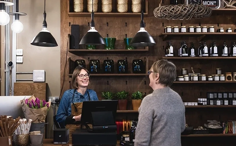 Kunde steht an einer ladentheke während ein mitarbeiter ein kassenterminal bedient in einem geschäft mit regalen voller produkte